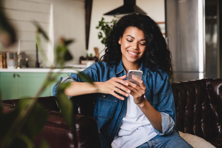 Relaxed young african woman texting on her phone in the modern house